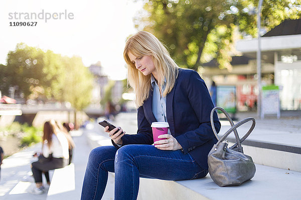 Blonde Geschäftsfrau mit Kaffee zum Anschauen von Smartphones