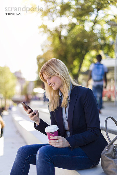Lächelnde Geschäftsfrau mit Kaffee zum Anschauen von Smartphones