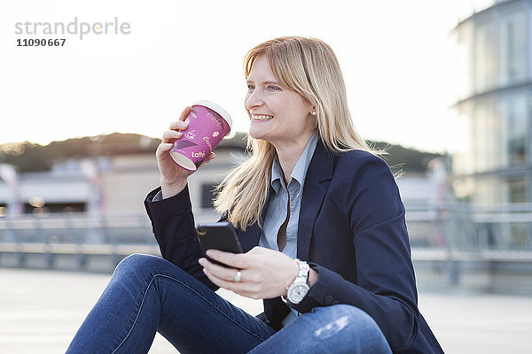 Lächelnde blonde Geschäftsfrau mit Smartphone und Kaffee zum Mitnehmen