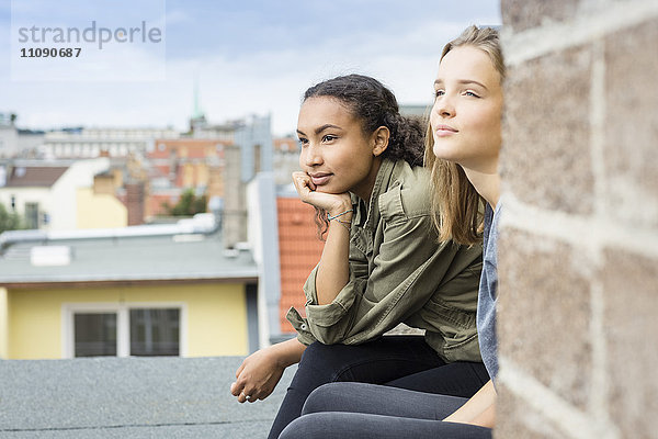 Zwei Teenager-Mädchen sitzen auf dem Dach und schauen in die Ferne.