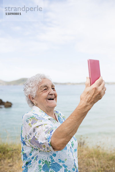 Fröhliche Seniorin mit Selfie am Strand