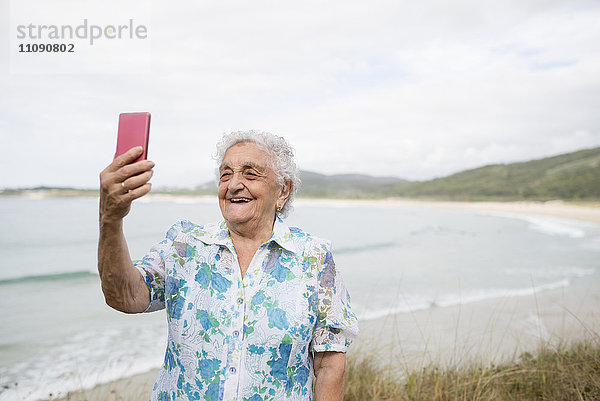 Fröhliche Seniorin mit Selfie am Strand