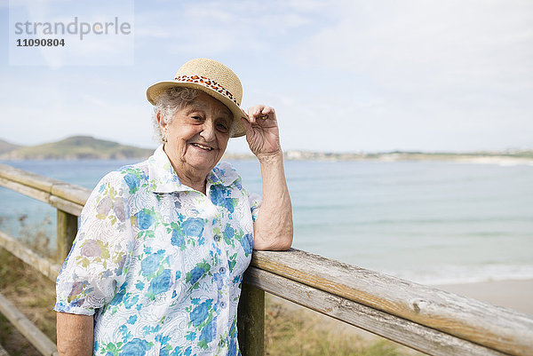Glückliche Seniorin mit Strohhut auf der Promenade stehend