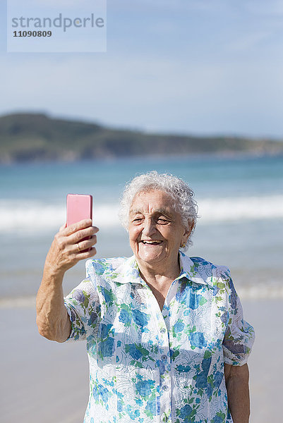 Fröhliche Seniorin mit Selfie am Strand