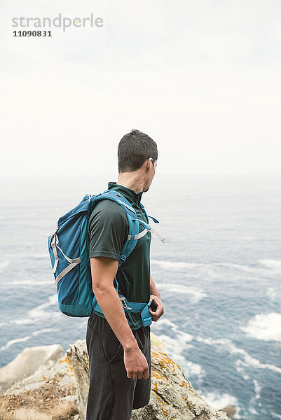 Junger Mann mit Rucksack vor dem Meer an der Küste