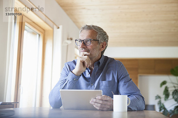 Erwachsener Mann mit digitalem Tablett auf dem Tisch zu Hause