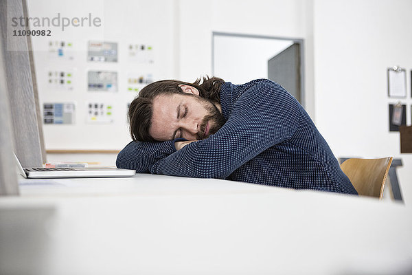 Mann schläft auf dem Schreibtisch im Büro
