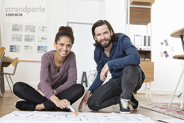 Porträt von zwei lächelnden Kollegen im Bürogeschoss mit Bauplan