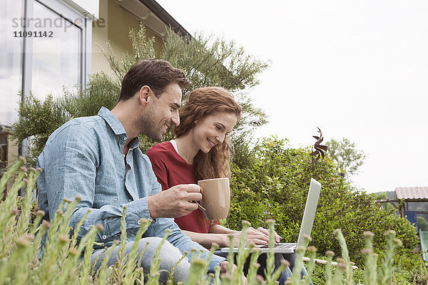 Lächelndes Paar im Garten sitzend mit Laptop