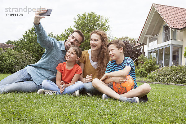 Lächelnde Familie  die im Garten sitzt und einen Selfie nimmt.