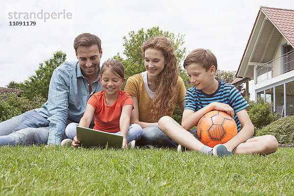Lächelnde Familie sitzend im Garten mit Fußball mit Tablette