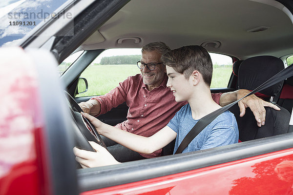 Vater unterrichtet den Sohn beim Autofahren