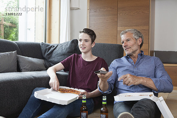 Vater und Sohn essen Pizza und sehen zusammen fern.