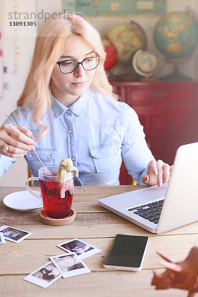 Frau  die zu Hause am Laptop arbeitet und Tee mit einem Zuckerstab rührt