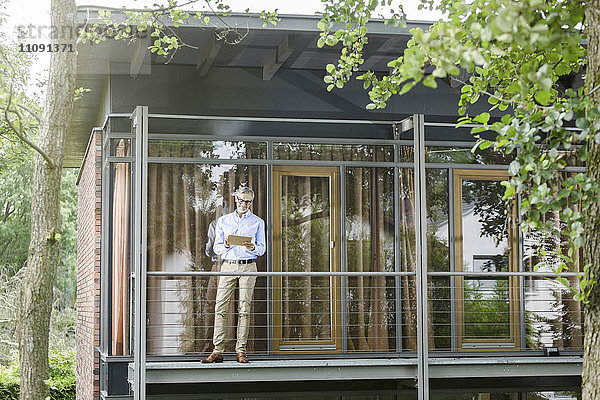 Mann steht auf dem Balkon seines Hauses mit Tablette
