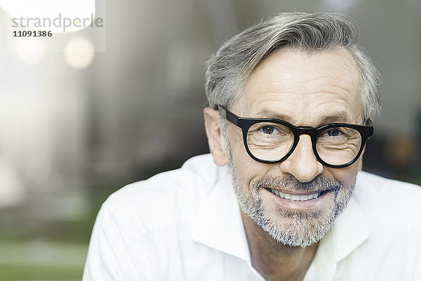 Porträt eines lächelnden Mannes mit grauen Haaren und Bart mit Brille