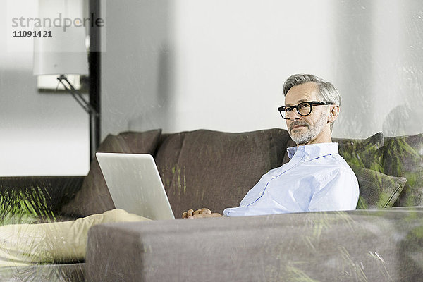 Mann sitzt auf der Couch in seinem Wohnzimmer mit Laptop