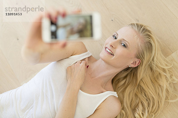 Blonde Frau auf Holzfußboden liegend  mit einem Selfie