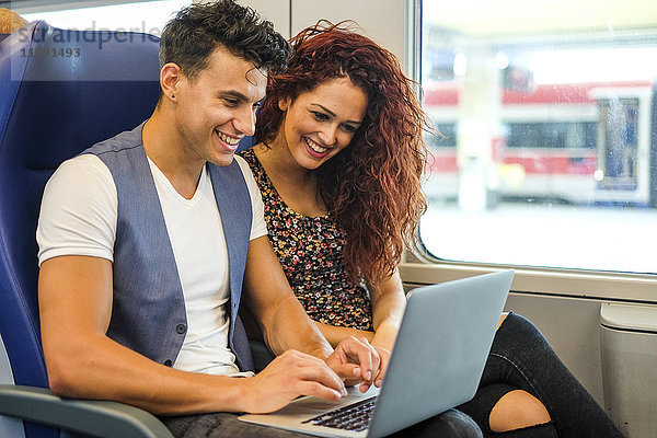 Lächelndes junges Paar im Zug mit Laptop
