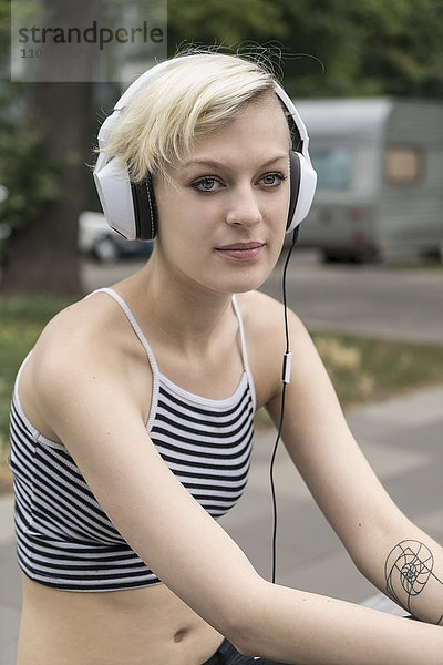 Porträt einer blonden jungen Frau beim Musikhören mit Kopfhörern