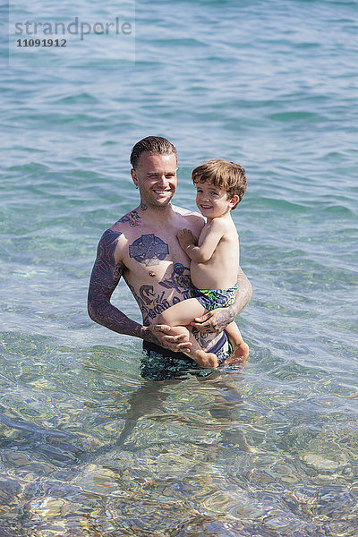 Tätowierter Mann mit seinem Sohn im Meer