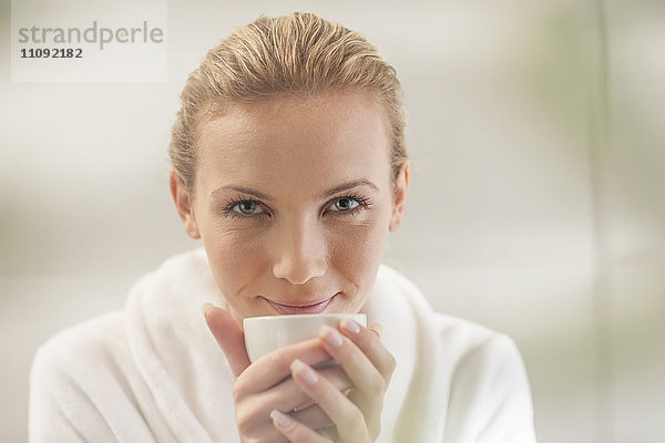Porträt der lächelnden jungen Frau im Bademantel beim Tee trinken