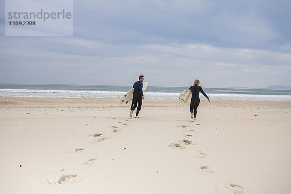 Paar mit Surfbrettern am Strand zu Fuß zum Meer