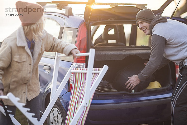 Glückliches Paar  das bei Sonnenuntergang seine Sachen im Auto packt.