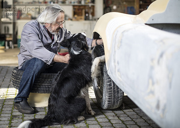 Senior Mann mit Hund untersucht Autoreifen