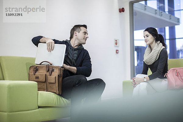 Junge Frau und Mann beim Herausnehmen des Laptops aus der Tasche in der Lobby