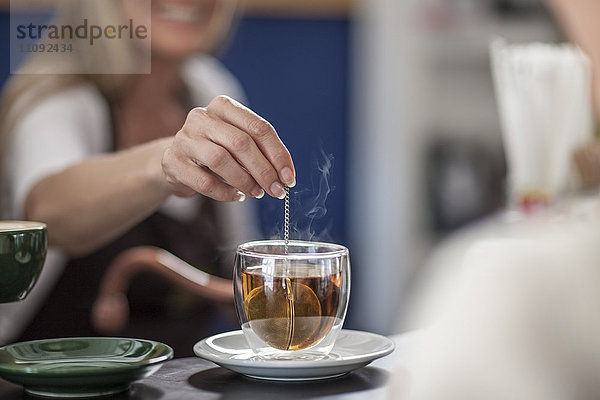 Frau in einem Café  die ein Glas Tee zubereitet.