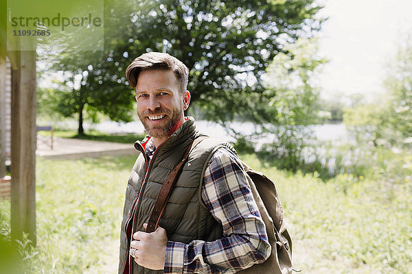 Portrait lächelnder Wanderer mit Rucksack im sonnigen Wald