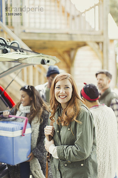 Portrait lächelnde Frau mit Freunden beim Entladen der Kühlbox vom Heck des Autos