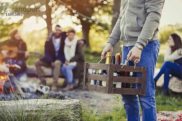 Mann mit Wein- und Bierkiste auf dem Campingplatz mit Freunden