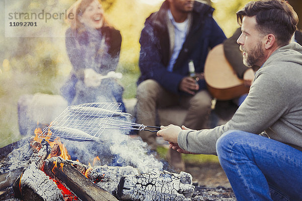 Mann frittiert Fisch im Grillkorb über dem Lagerfeuer bei Freunden