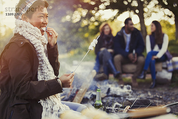 Lächelnde Frau beim Essen von gebratenen Marshmallows am Lagerfeuer