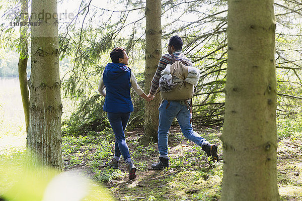 Paar beim Händchenhalten und Wandern mit Rucksack im Wald