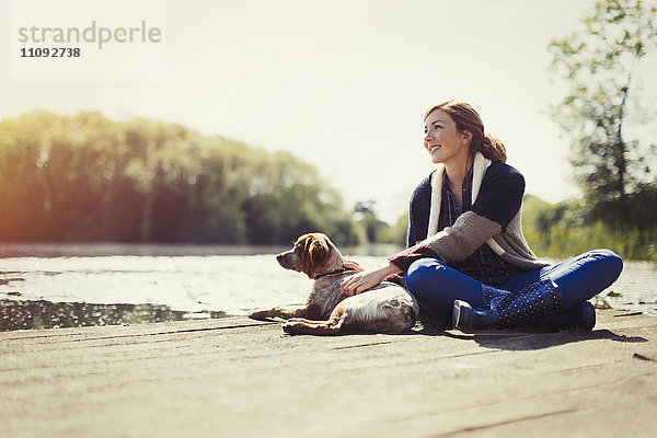 Lächelnde Frau und Hund entspannen sich am sonnigen Seeufer.