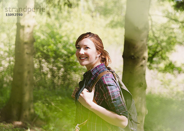 Lächelnde Frau mit Rucksackwandern im sonnigen Wald