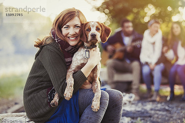 Portrait lächelnde Frau umarmt Hund auf dem Campingplatz mit Freunden