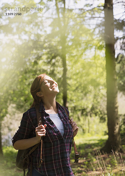 Gelassene Frau  die sich im Sonnenlicht sonnt und im Wald wandert.