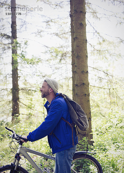 Mann mit Rucksack und Mountainbike im sonnigen Wald