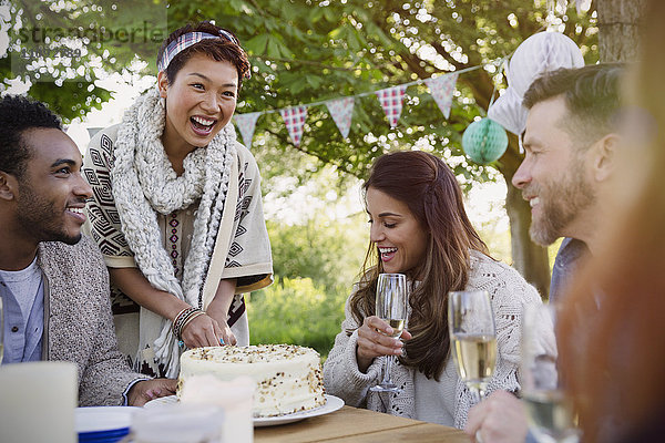 Lächelnde Freunde trinken Champagner und schneiden Geburtstagskuchen auf der Terrasse.