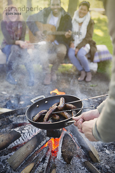 Freunde kochen Hot Dogs am Lagerfeuer