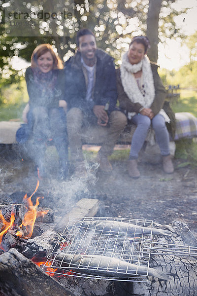 Freunde beobachten Fischkochen im Grillkorb am Lagerfeuer