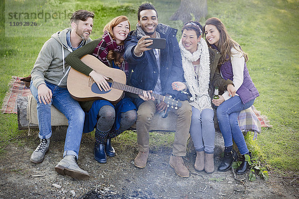 Freunde mit Gitarre nehmen Selfie mit Fotohandy auf dem Campingplatz mit.