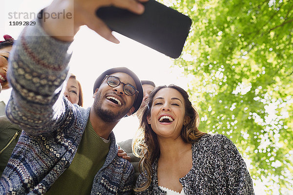 Enthusiastische Freunde nehmen Selfie mit Kamera-Handy unter Baum