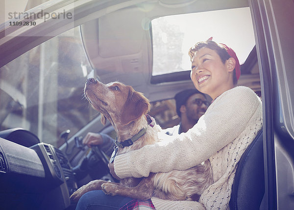 Lächelnde Frau hält Hund auf Schoß im Auto