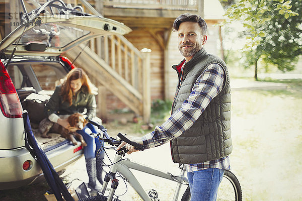 Portrait lächelnder Mann mit Mountainbike in der Nähe des Autos hinter der Hütte