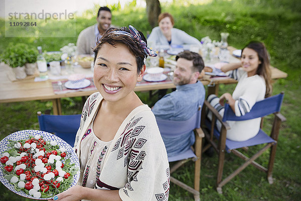 Portrait lächelnde Frau serviert Caprese-Salat an Freunde am Gartenparty-Tisch